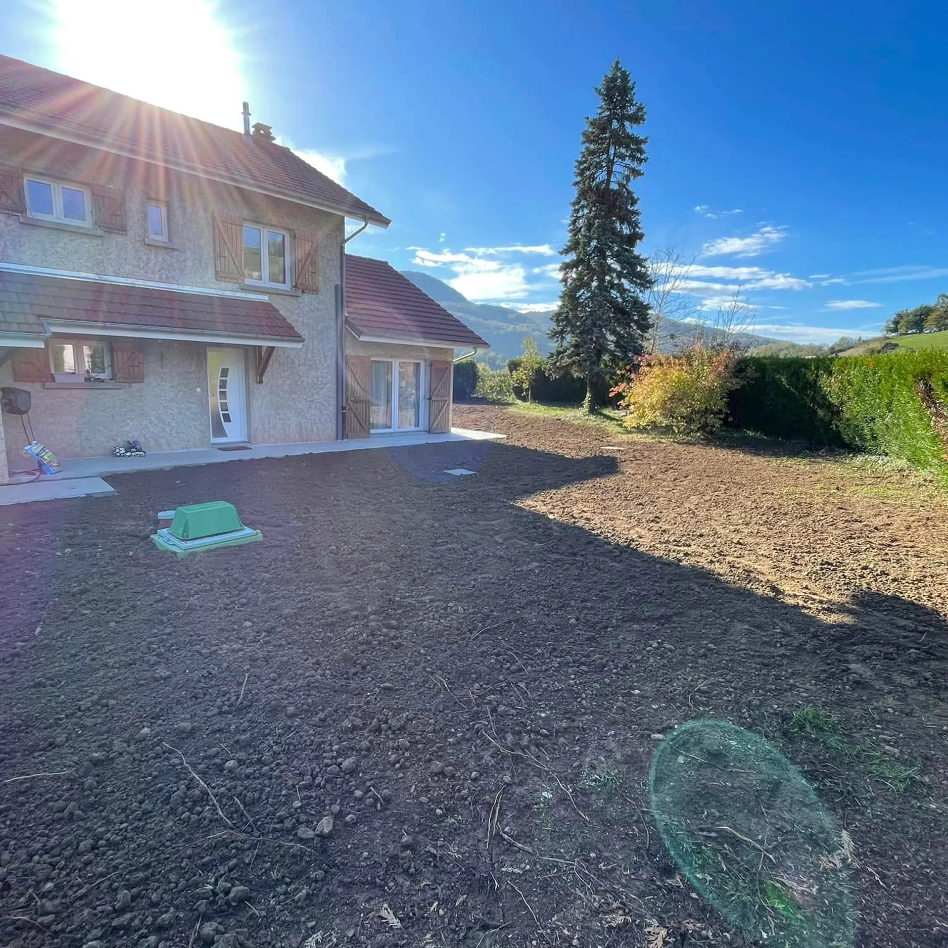 Un jardin avec une cuve verte installée dans le sol, entouré de végétation.